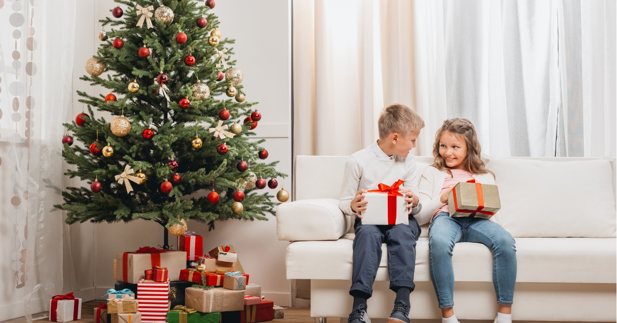 Děti sedí u vánočního stromku s dárky
